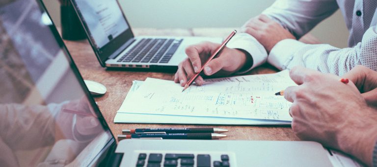 men at desk with paper, pencil, laptops - running a sales promotion for supplements